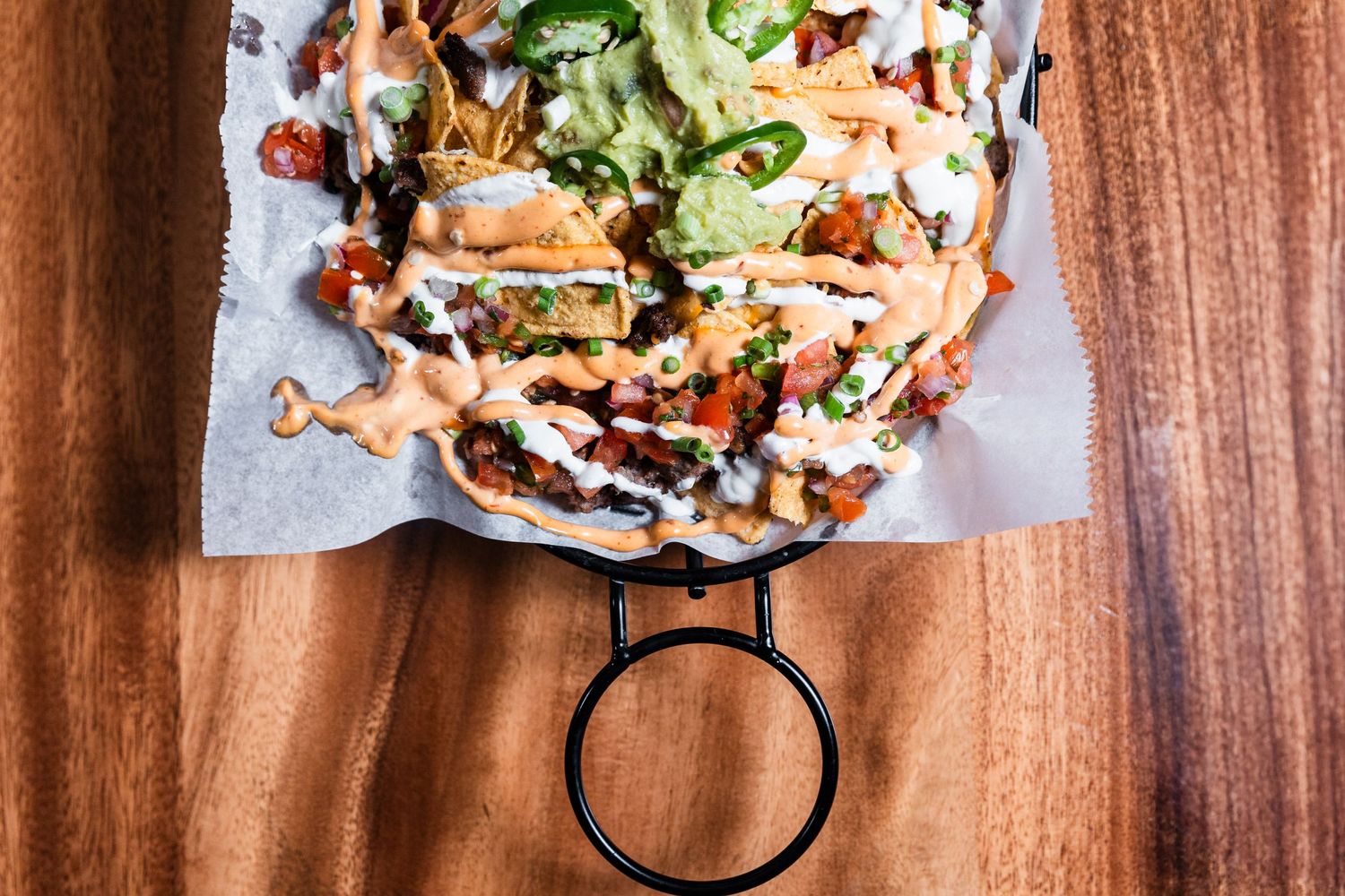 Mexican-style loaded nachos with creamy sauce, jalapeños and fresh herbs on wooden serving board.