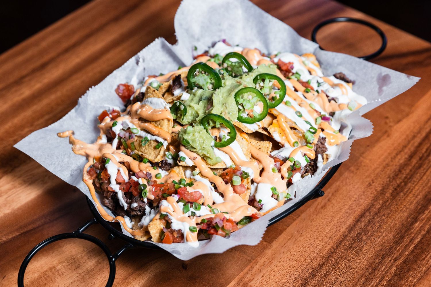 Crispy nachos loaded with jalapeños, cheese sauce and fresh toppings served on white paper.