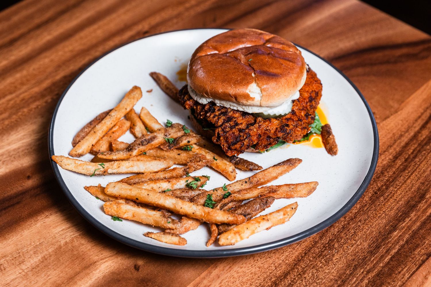 Gourmet burger with crispy french fries served on white plate against wooden surface.