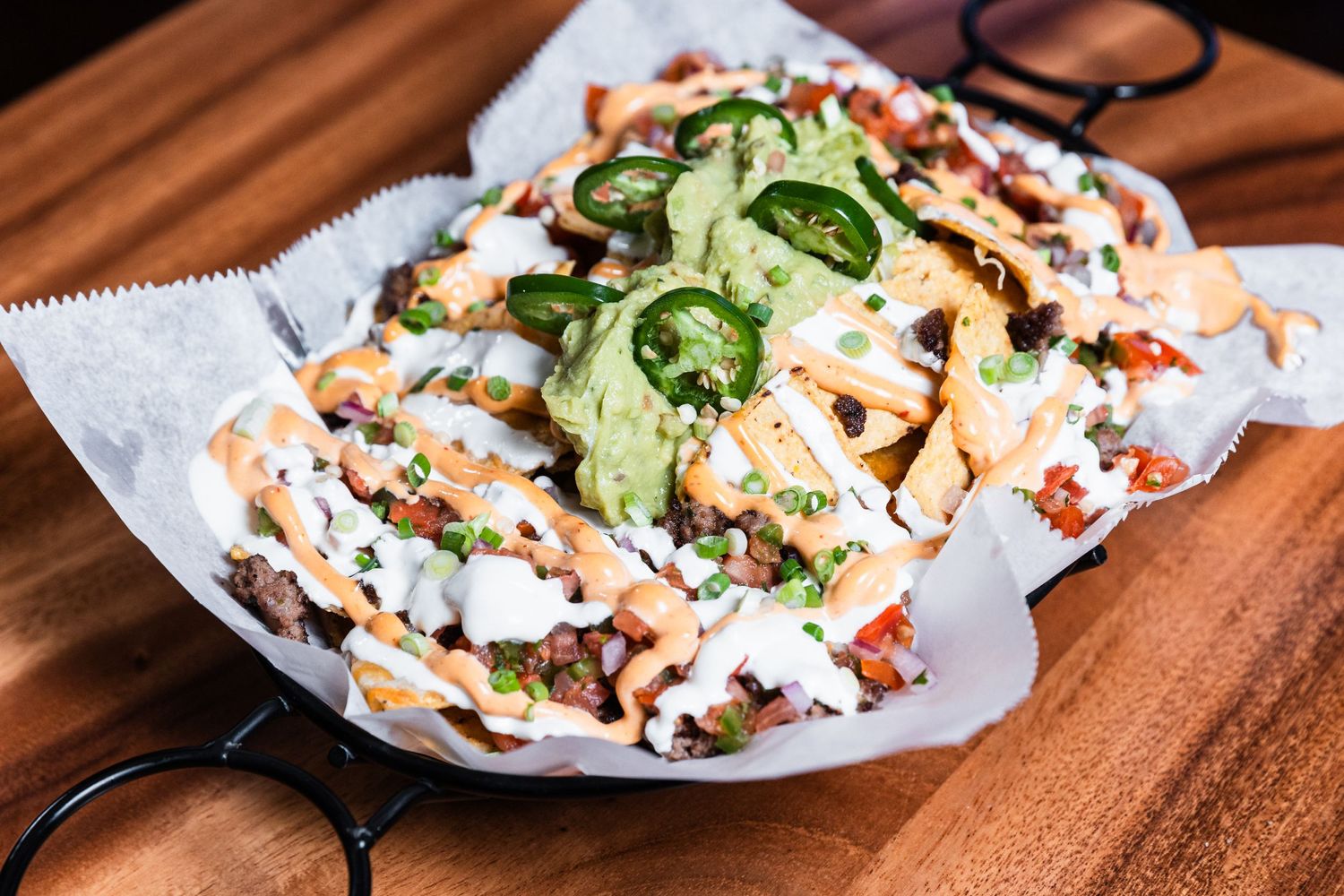 Loaded nachos topped with fresh avocado, cheese sauce and jalapeños on parchment paper.