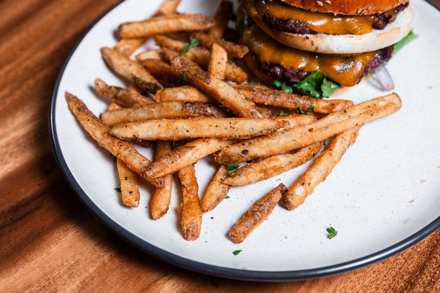 Golden crispy french fries garnished with fresh herbs served on a white plate with dark wood background.
