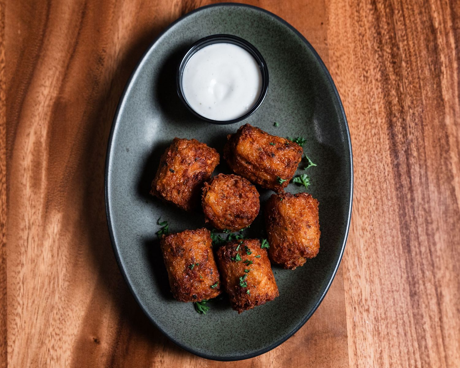 Crispy breaded appetizers served with white dipping sauce on dark plate against wooden surface.