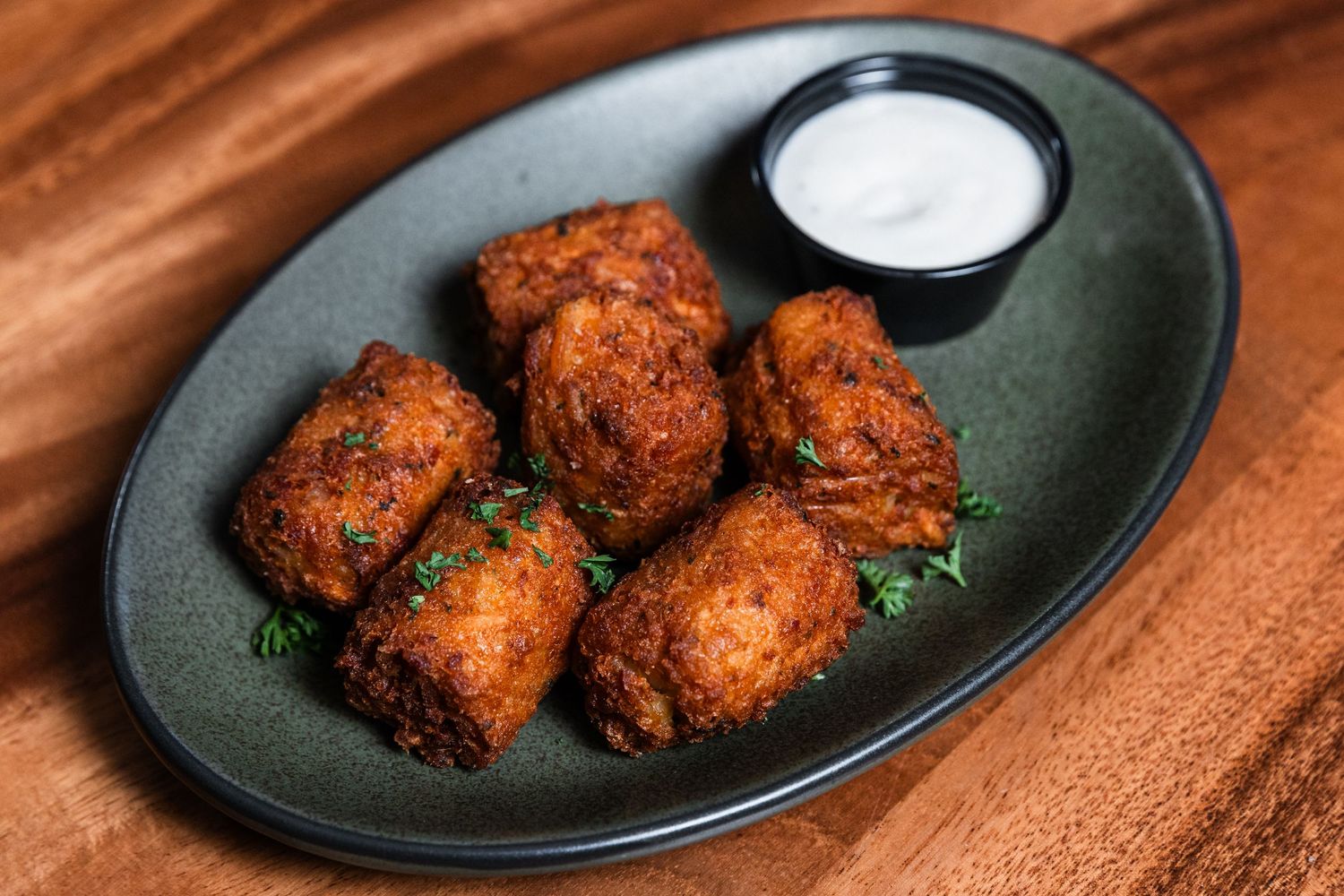 Golden brown breaded nuggets arranged on black plate with creamy dipping sauce and herb garnish.