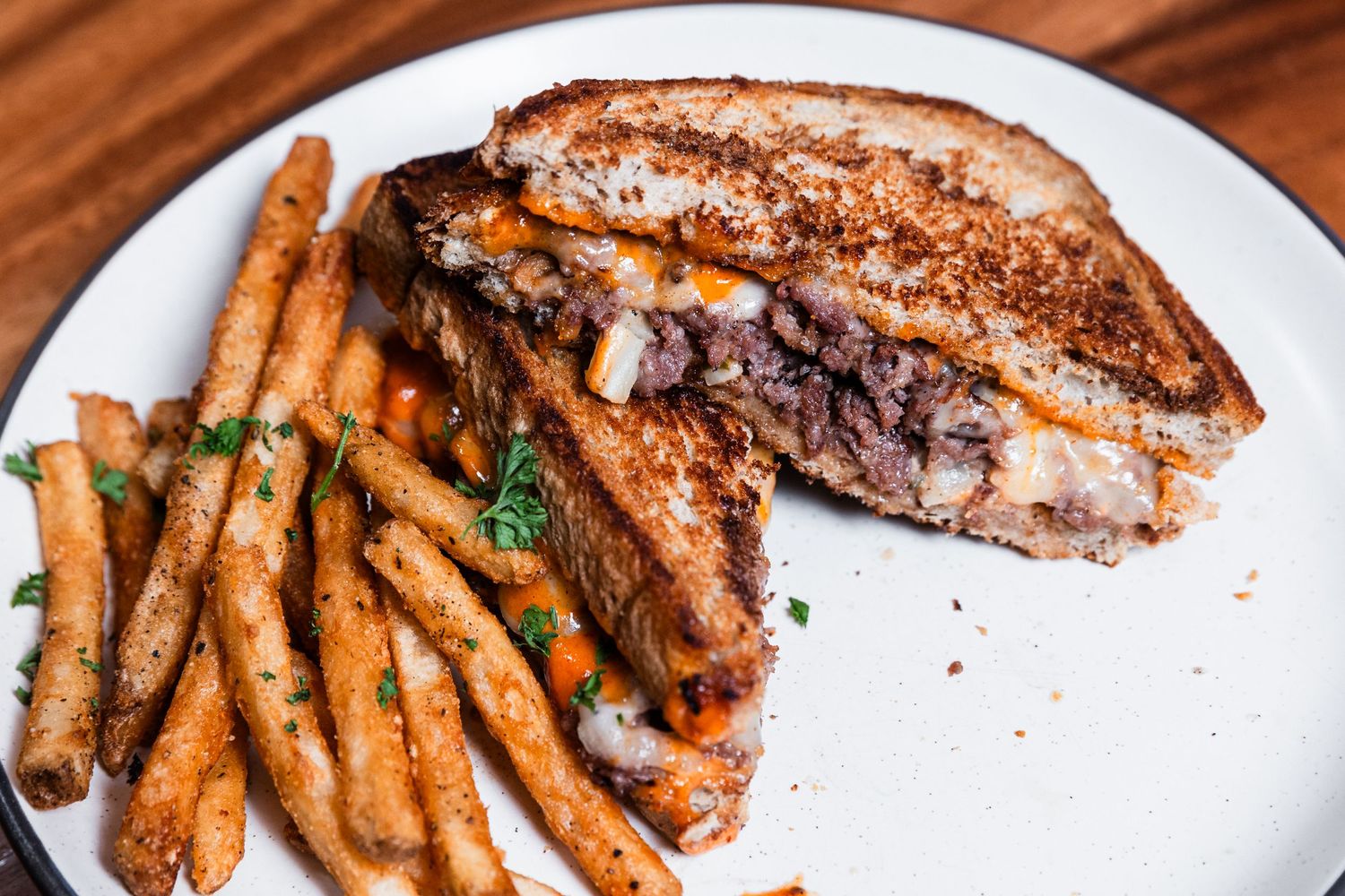 Close-up of grilled sandwich with melted interior and crispy french fries on white ceramic plate.