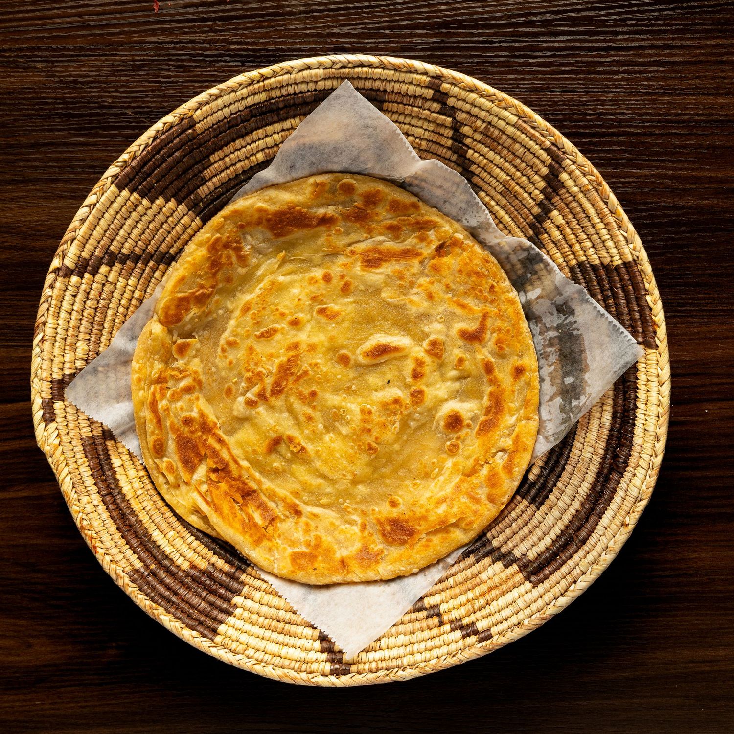 Golden flaky layered paratha bread served on woven basket plate.