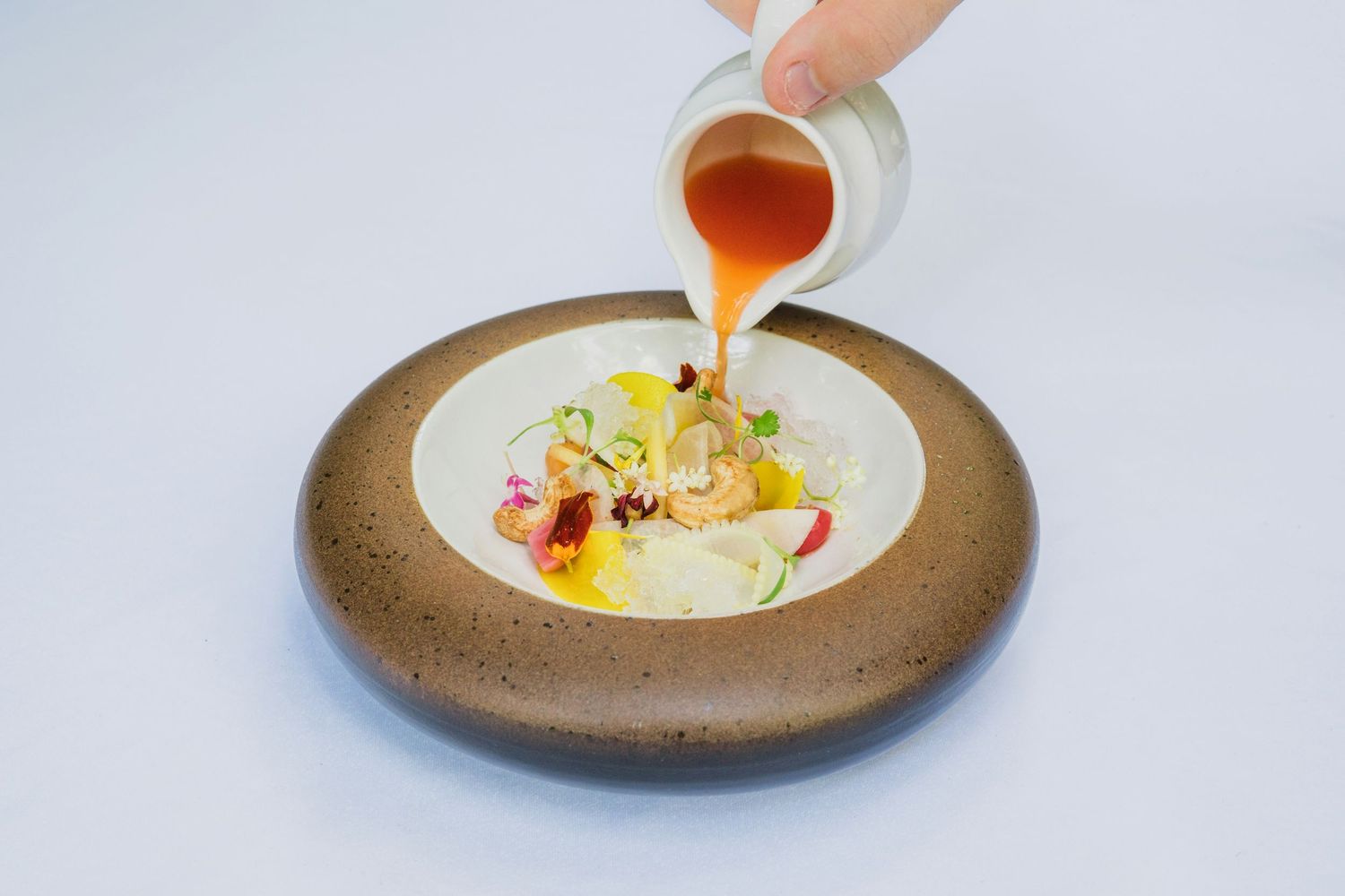 Chef adds finishing touches to an elegant plated dish with drizzled sauce and garnishes on a rustic ceramic plate.