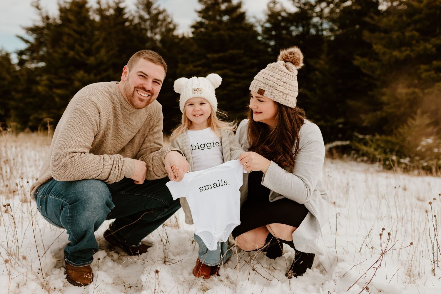 A family with their toddler daughter holding a gender reveal onesie, revealing their baby boy gender