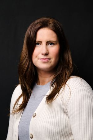 Professional headshot against black background wearing a white ribbed sweater and gray top.