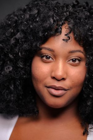 Close-up portrait with natural curly black hair and warm smile against blurred background.