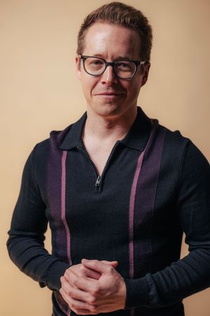 A sequence of studio portraits showing someone in a black zip-up sweater with pink accents against a beige background.