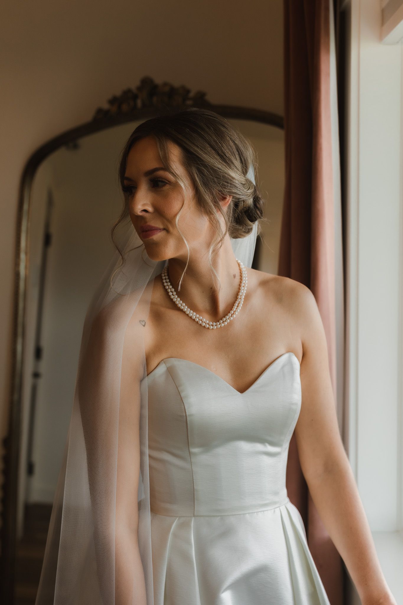 Elegant bridal portrait with pearl necklace and classic white wedding gown near vintage mirror. Spokane wedding photographer.