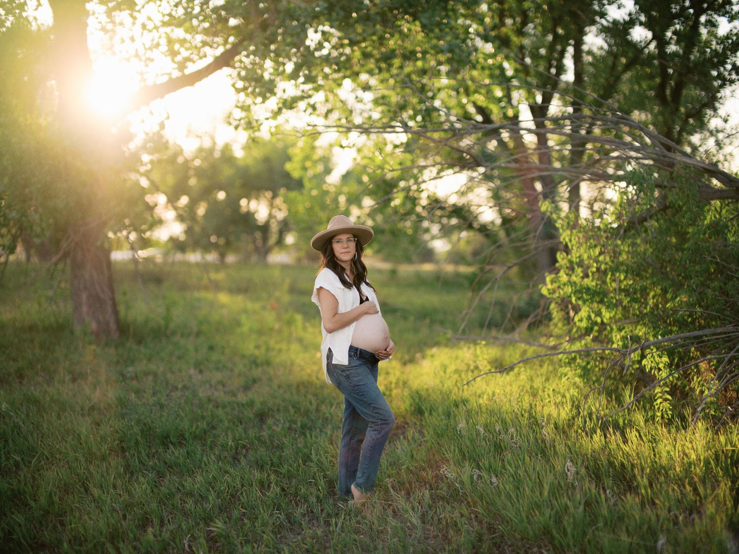 Woman in hat stands in sunlit field during golden hour nature photoshoot.