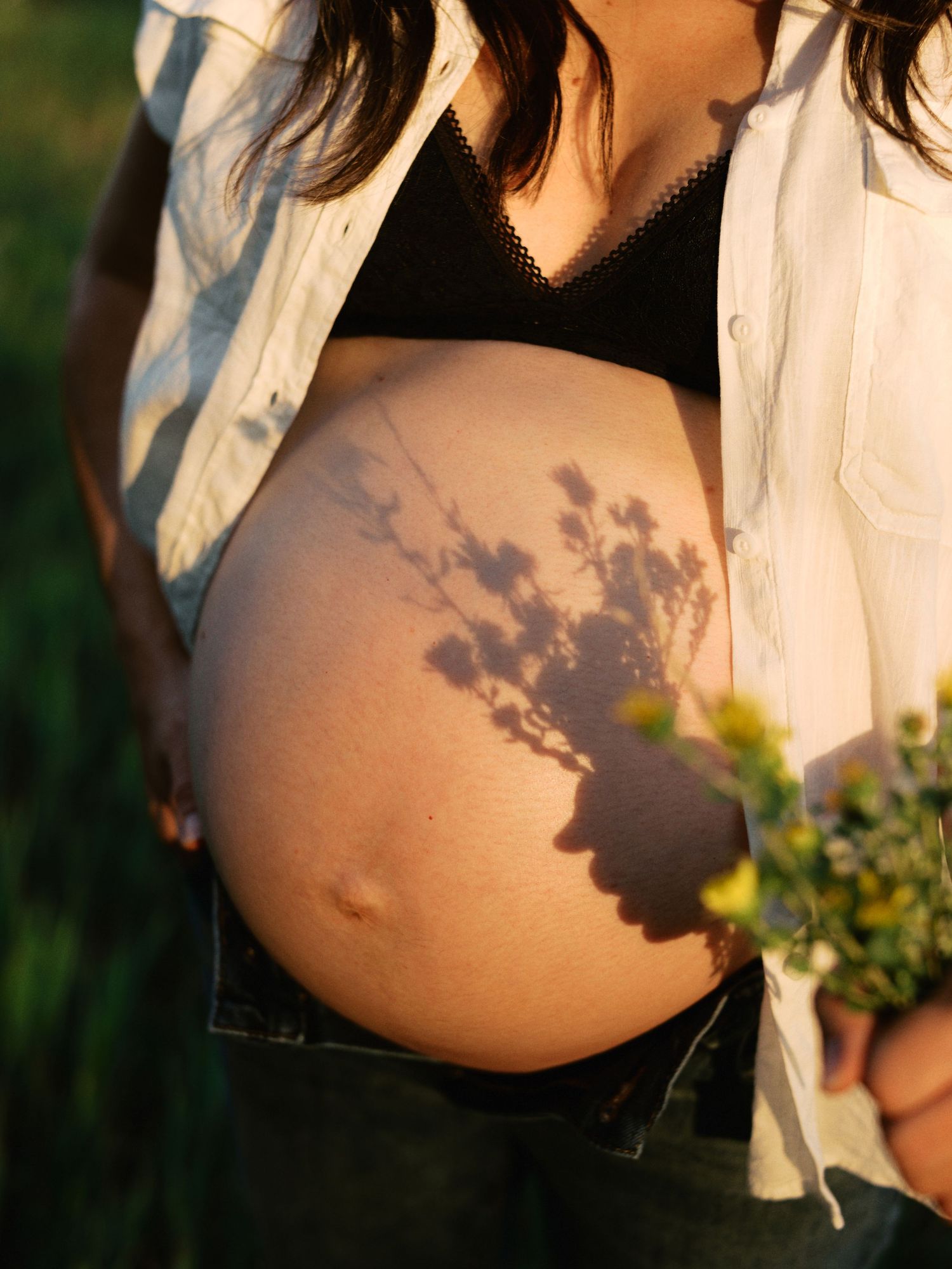 Beautiful shadow of tree branches cast on a pregnant belly in natural sunlight during an outdoor maternity photoshoot.
