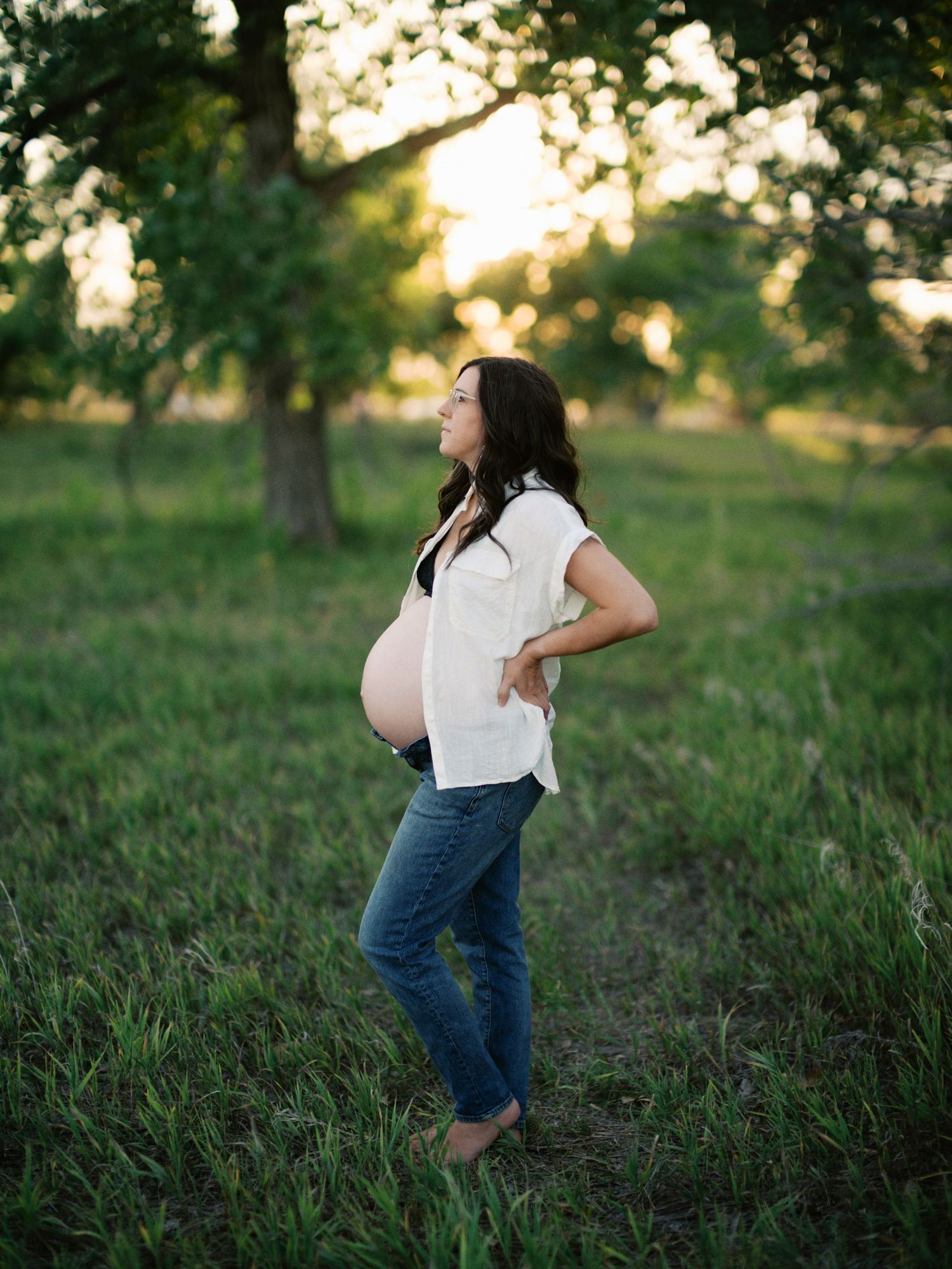 Side view maternity photo of expectant mother in white shirt and jeans during golden hour.
