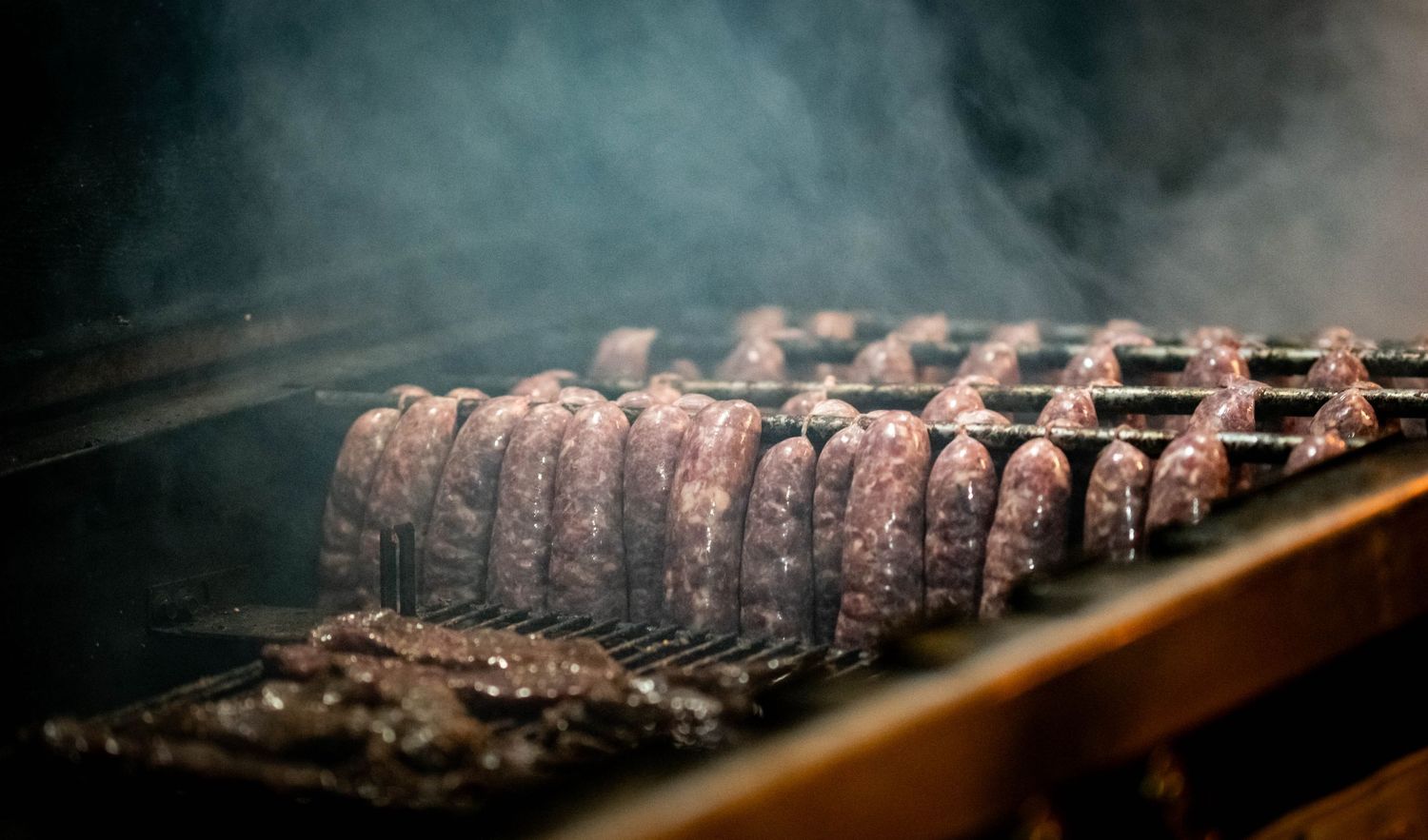 Smoked game meat sausages displayed in rows under atmospheric lighting.