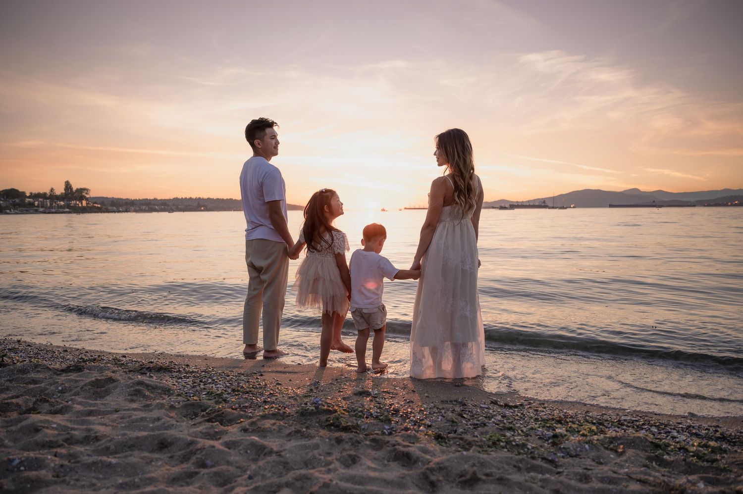 Silhouetted family stands together watching sunset over mountain beach landscape.