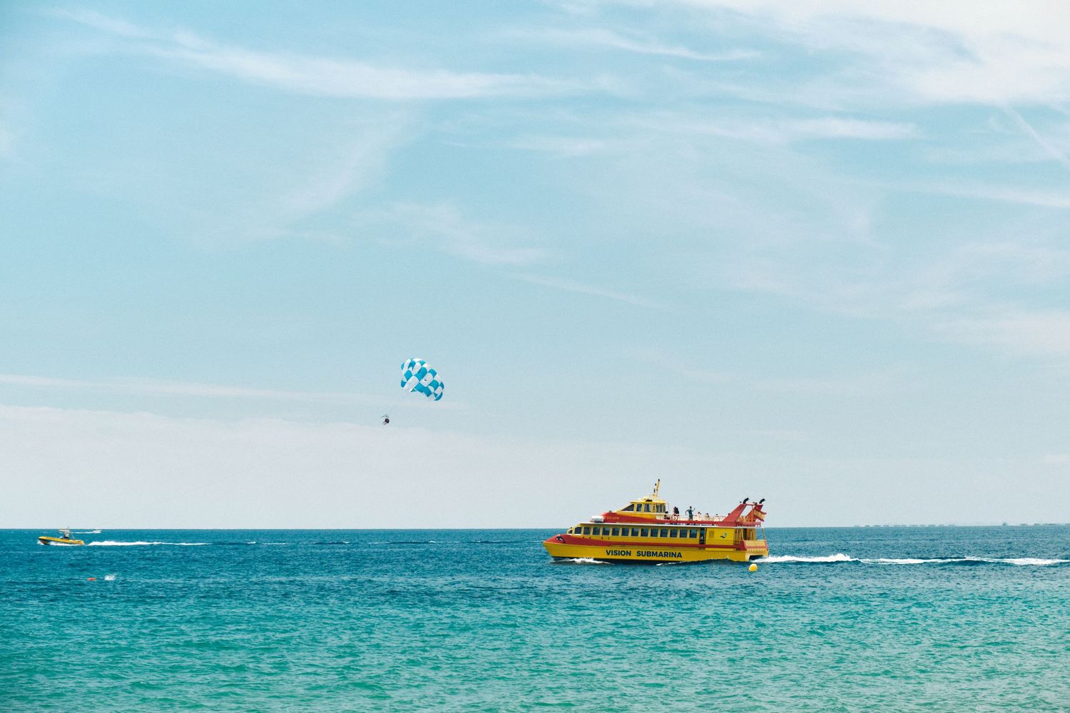 Yellow tourist boat cruising on bright blue waters with parasailing activity in the background.