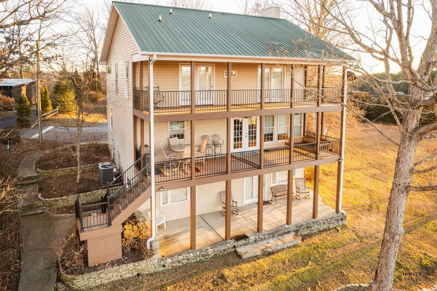 Panoramic view of a rustic farmhouse with wrap-around porch and green metal roof during autumn sunset.