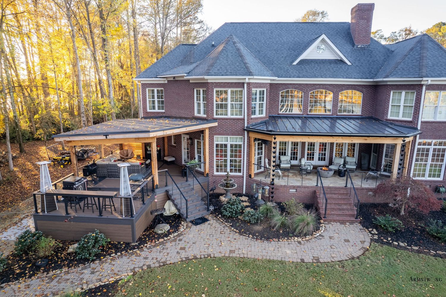 Elegant brick home exterior showcasing multiple angles and landscaping during autumn with golden foliage in background.