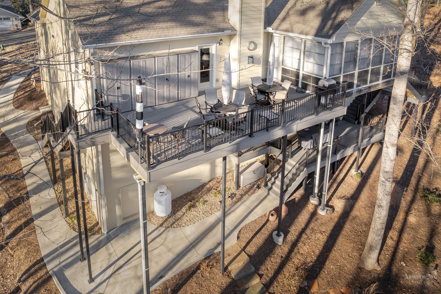 Modern outdoor deck with metal railings and seating area casting long shadows through trees in afternoon sunlight.
