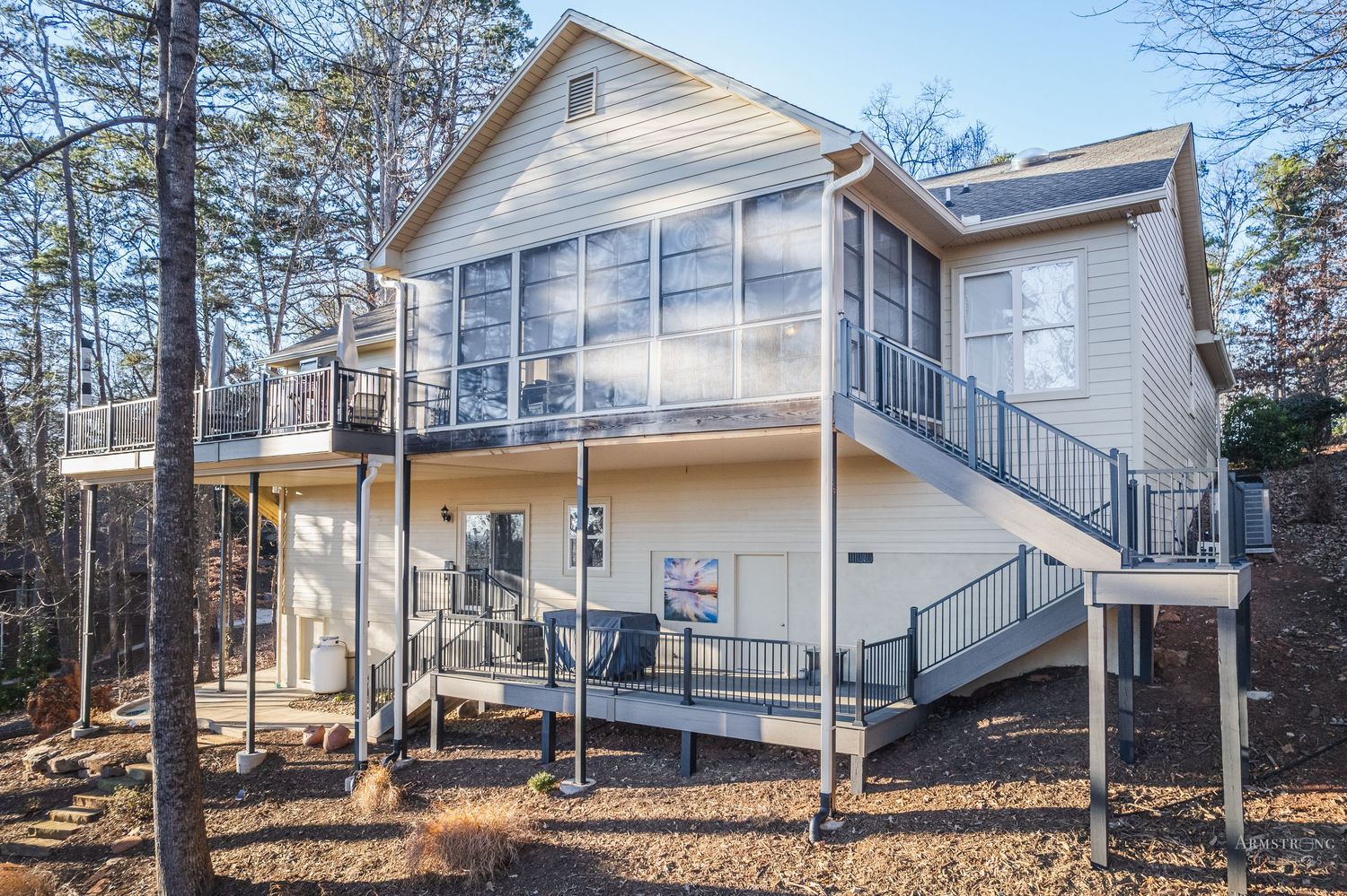 Modern white residential home exterior with multiple levels and decks surrounded by autumn trees and fallen leaves.