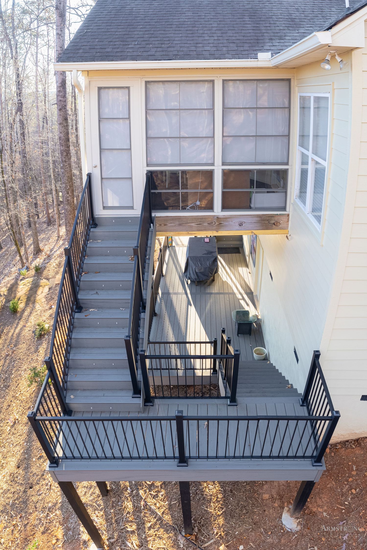 Modern multi-level deck with gray composite decking, black metal railings and screened porch on white house in wooded setting.