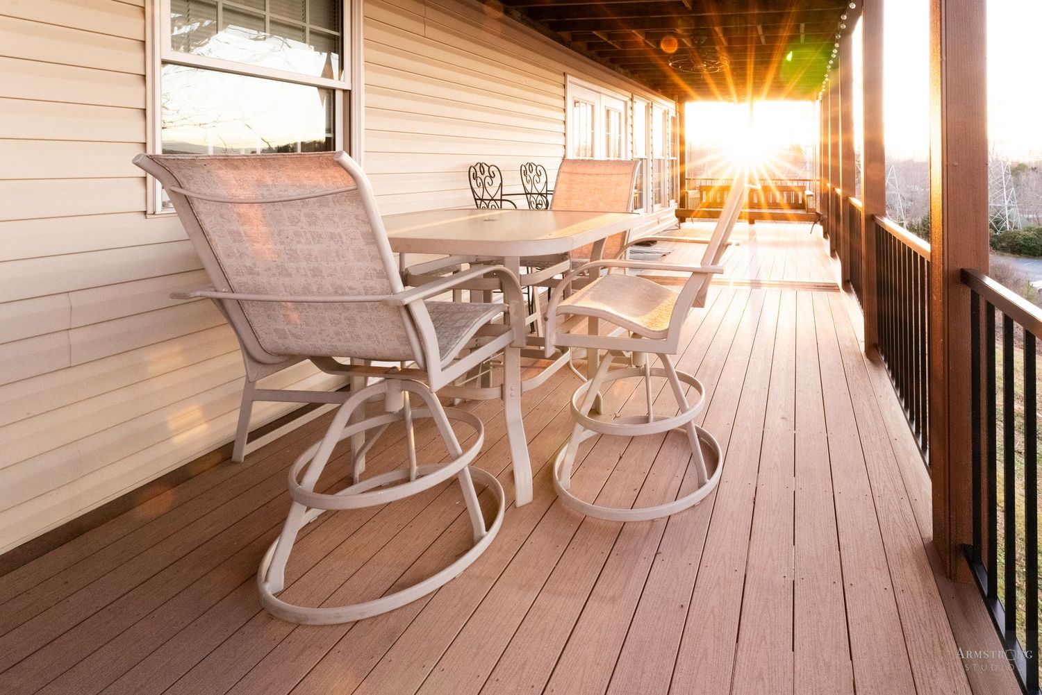 A wooden deck patio with white rocking chairs and warm sunlight filtering through creating a cozy outdoor seating area.
