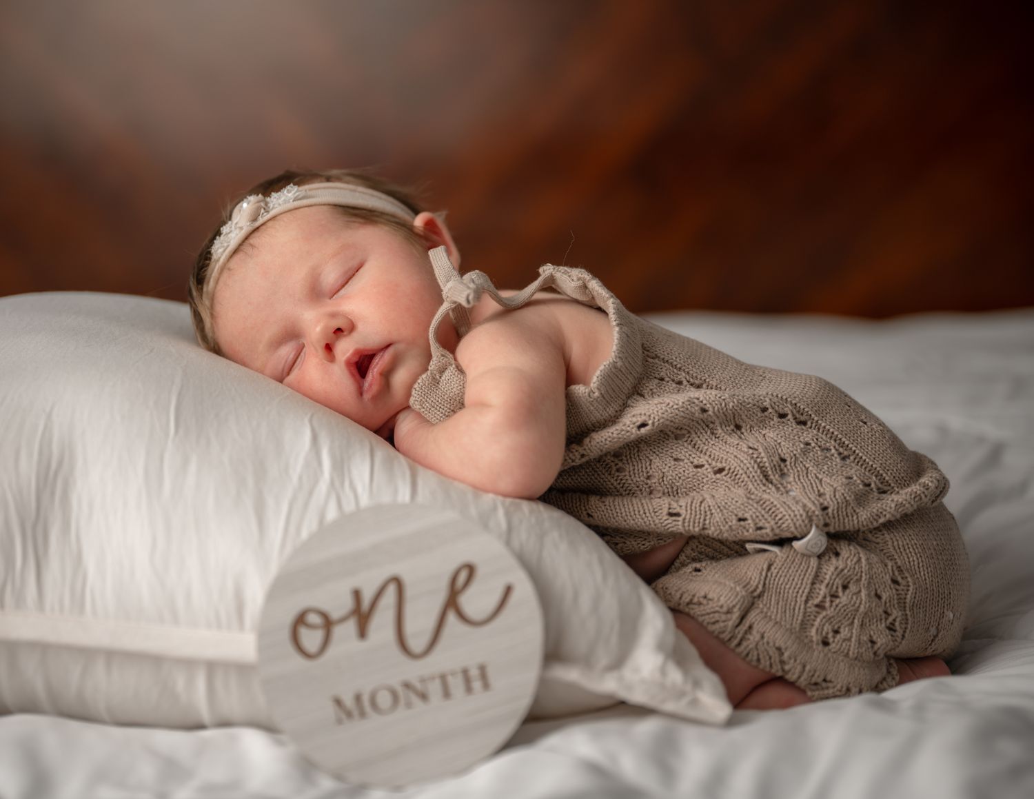 One month old baby sleeping on pillow in lace outfit.