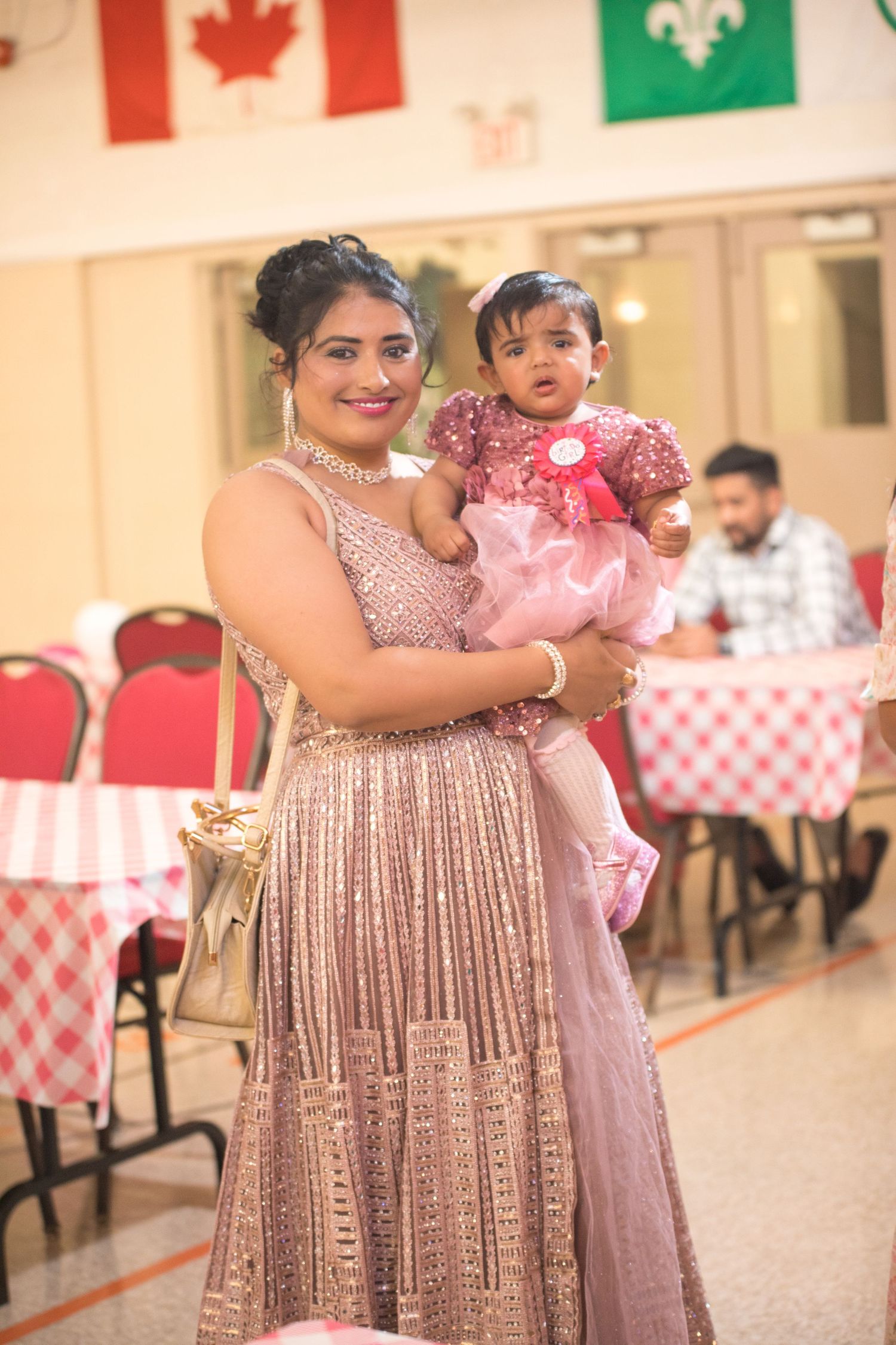 Woman in sparkly dress holding child in pink outfit at celebration with flags.