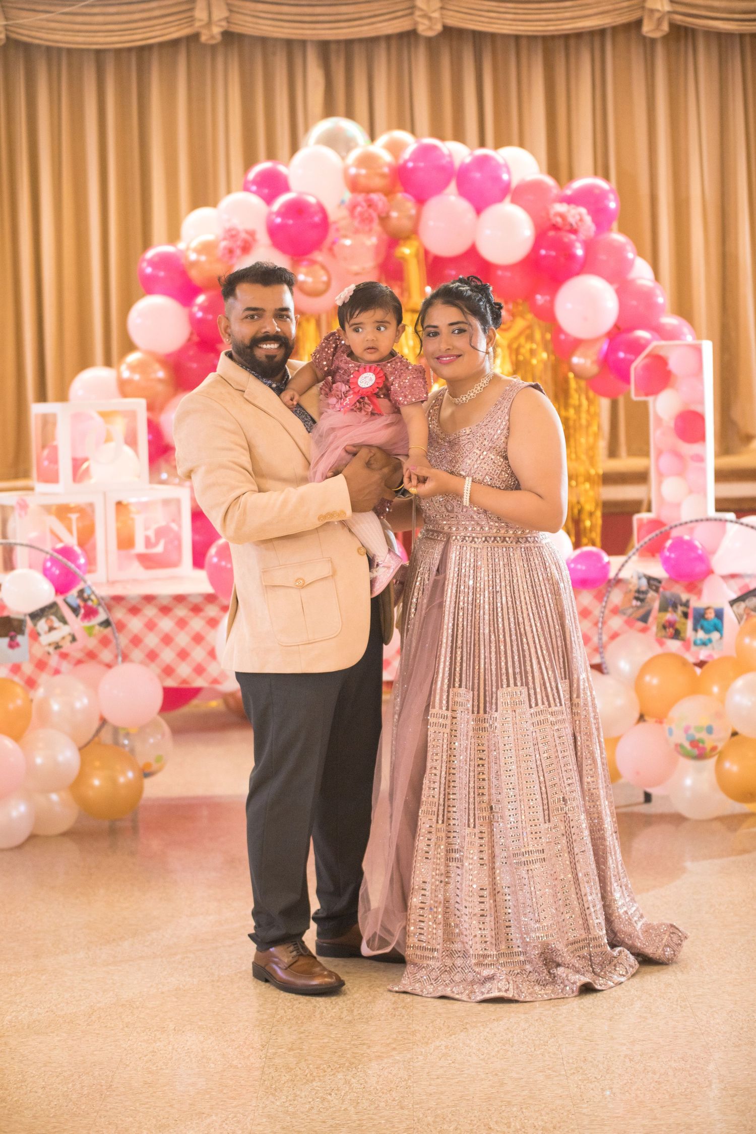 Family posing in formal attire against pink balloon arch and gold curtain backdrop.