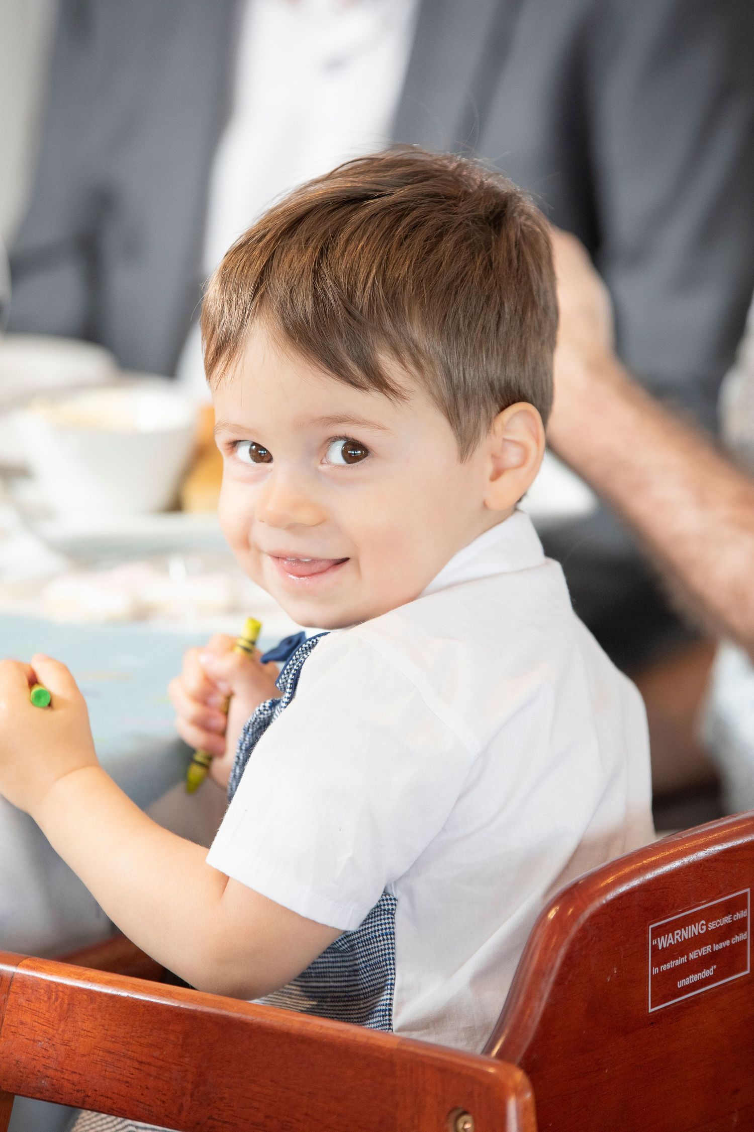 Young boy in white shirt smiling while seated at formal dining table.