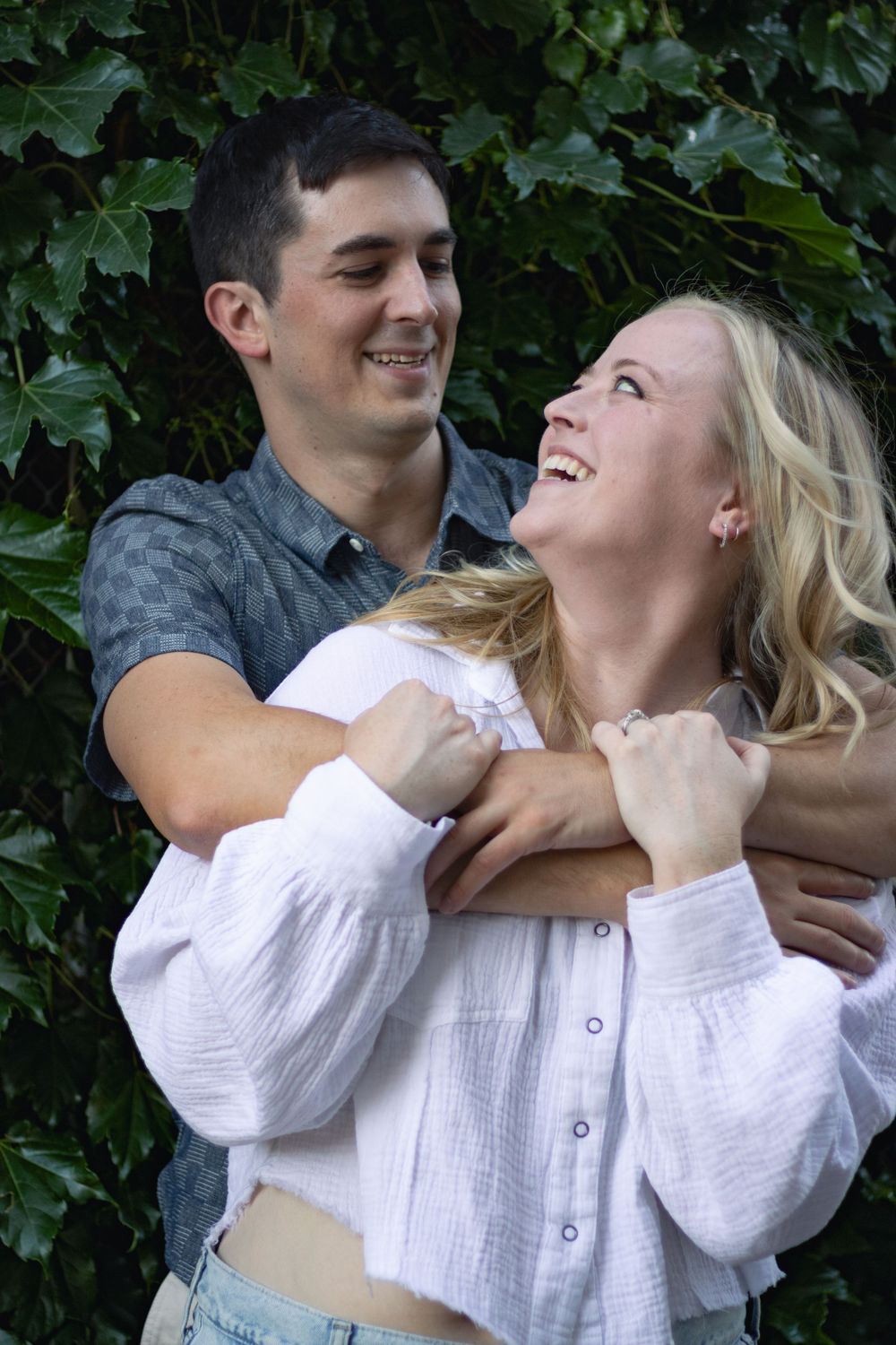 A couple shares playful moments against a backdrop of green ivy.