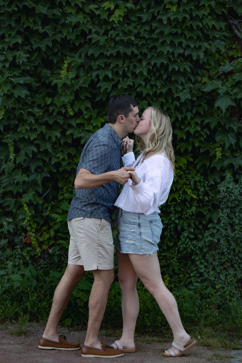 A couple shares an intimate moment in front of an ivy-covered wall.