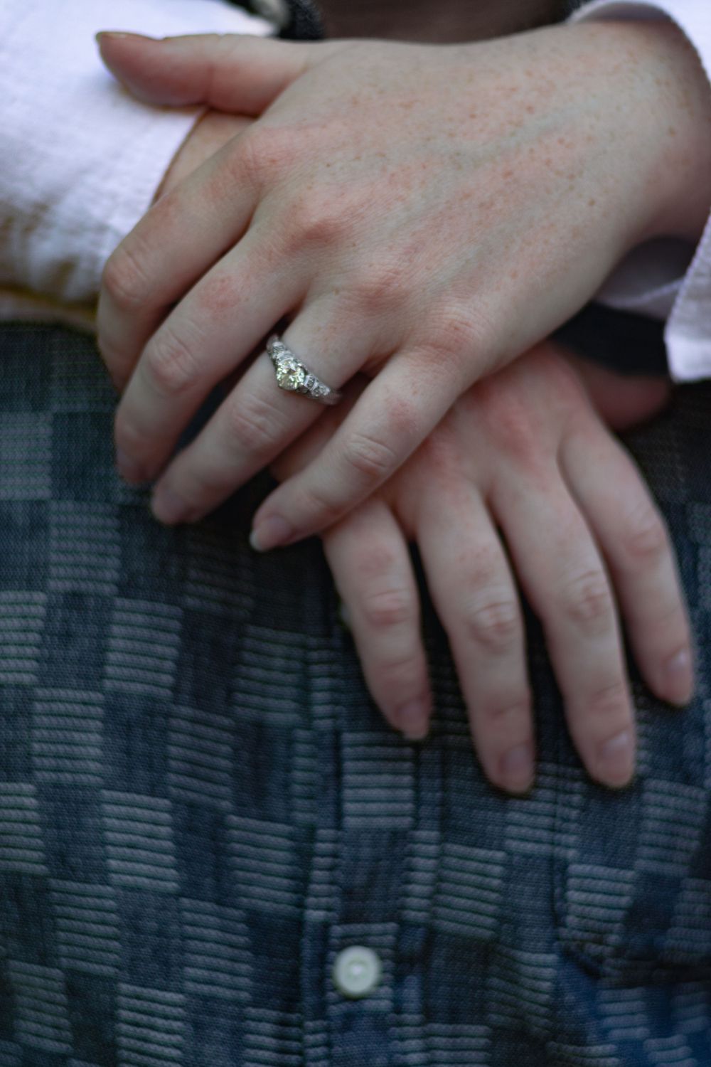 Close-up of hands with an engagement ring resting on textured fabric.