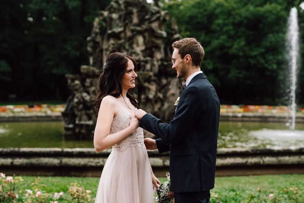 Romantic wedding couple shares tender moments in front of garden fountain.