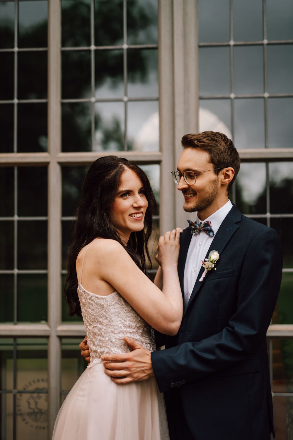 A couple shares playful moments against a backdrop of large windows.