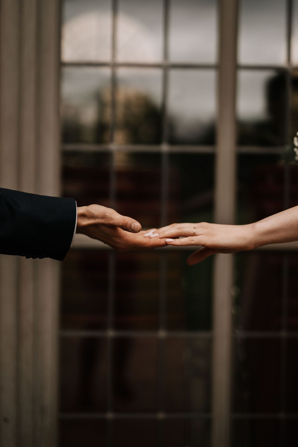 Two hands reaching toward each other against a window backdrop in an intimate moment.