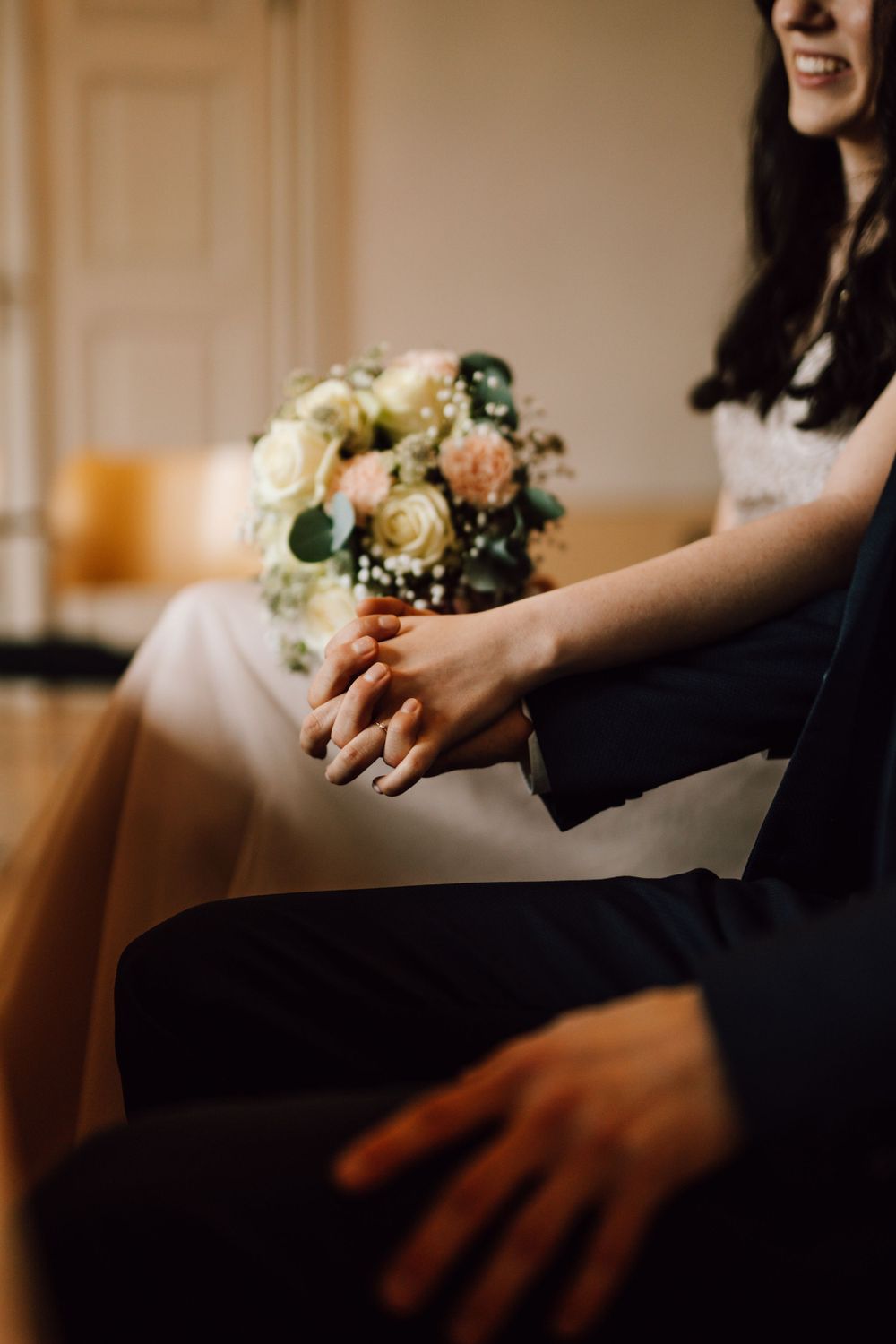 A bouquet of pink and white roses rests beside elegantly dressed wedding attendees.
