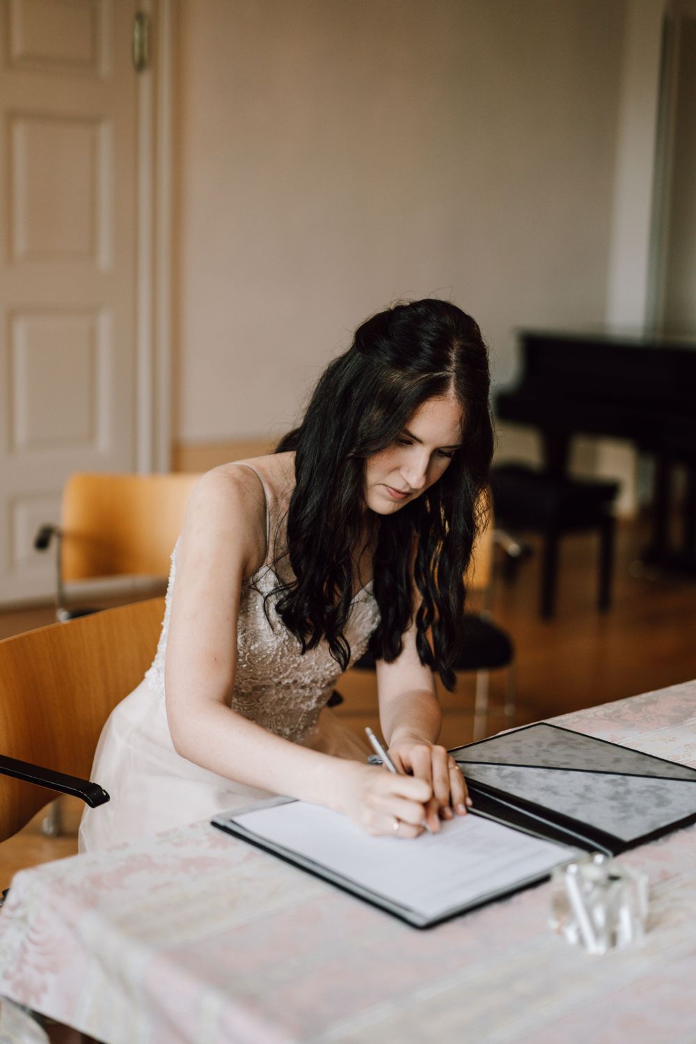 A person in a white dress signs documents at a formal table.