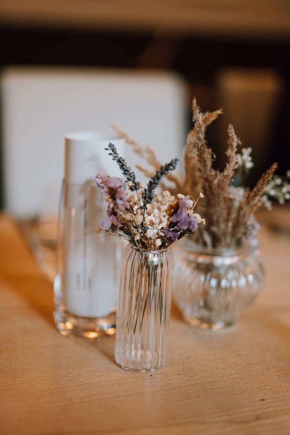 Small glass vases with delicate dried flowers and lavender arranged on a wooden table.