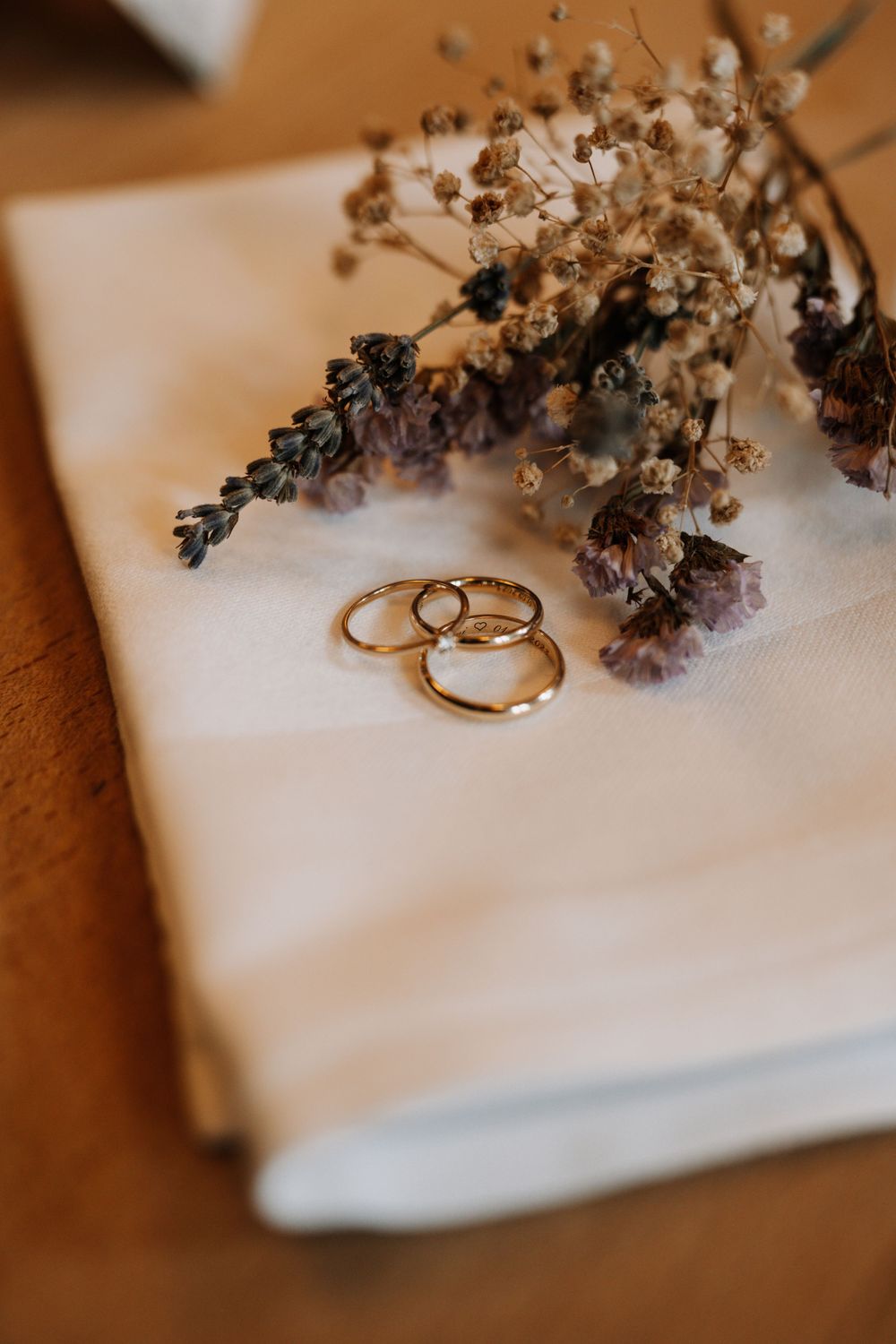 Gold wedding bands nestled among dried flowers on a white linen napkin.