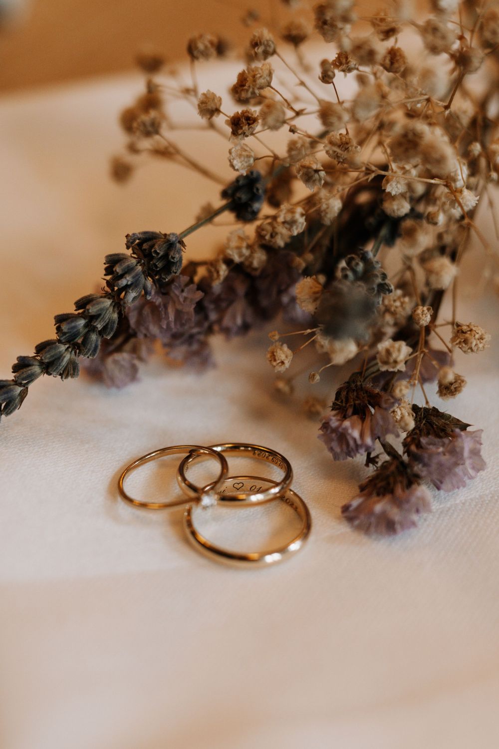 Wedding rings displayed artistically with dried flowers on a white surface.