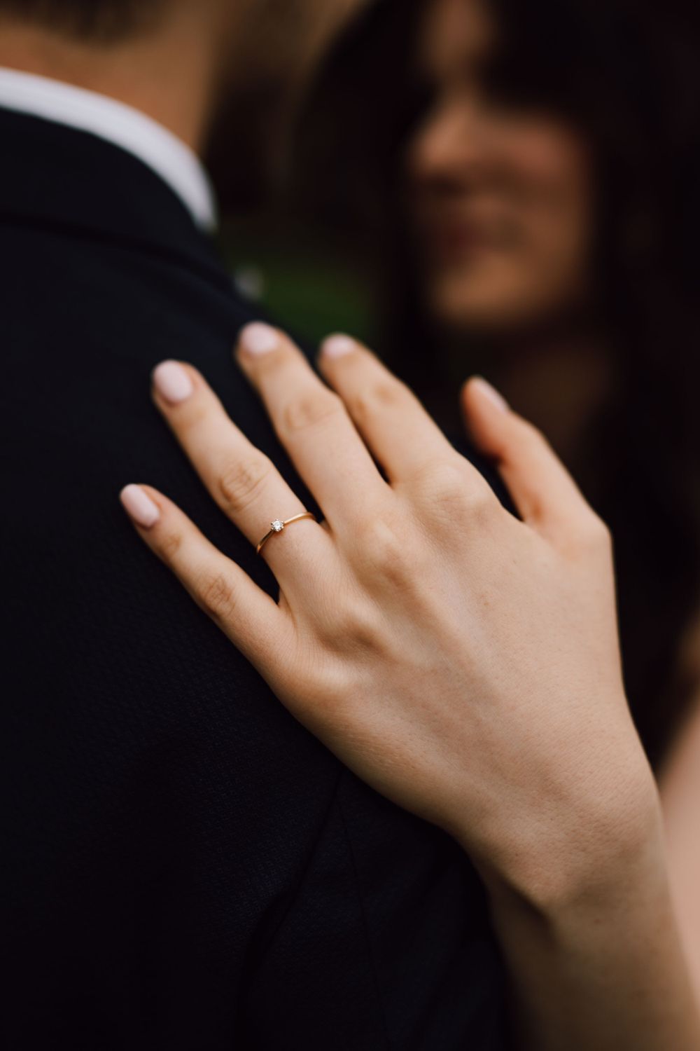 Close-up of a delicate wedding ring on hand against dark background.