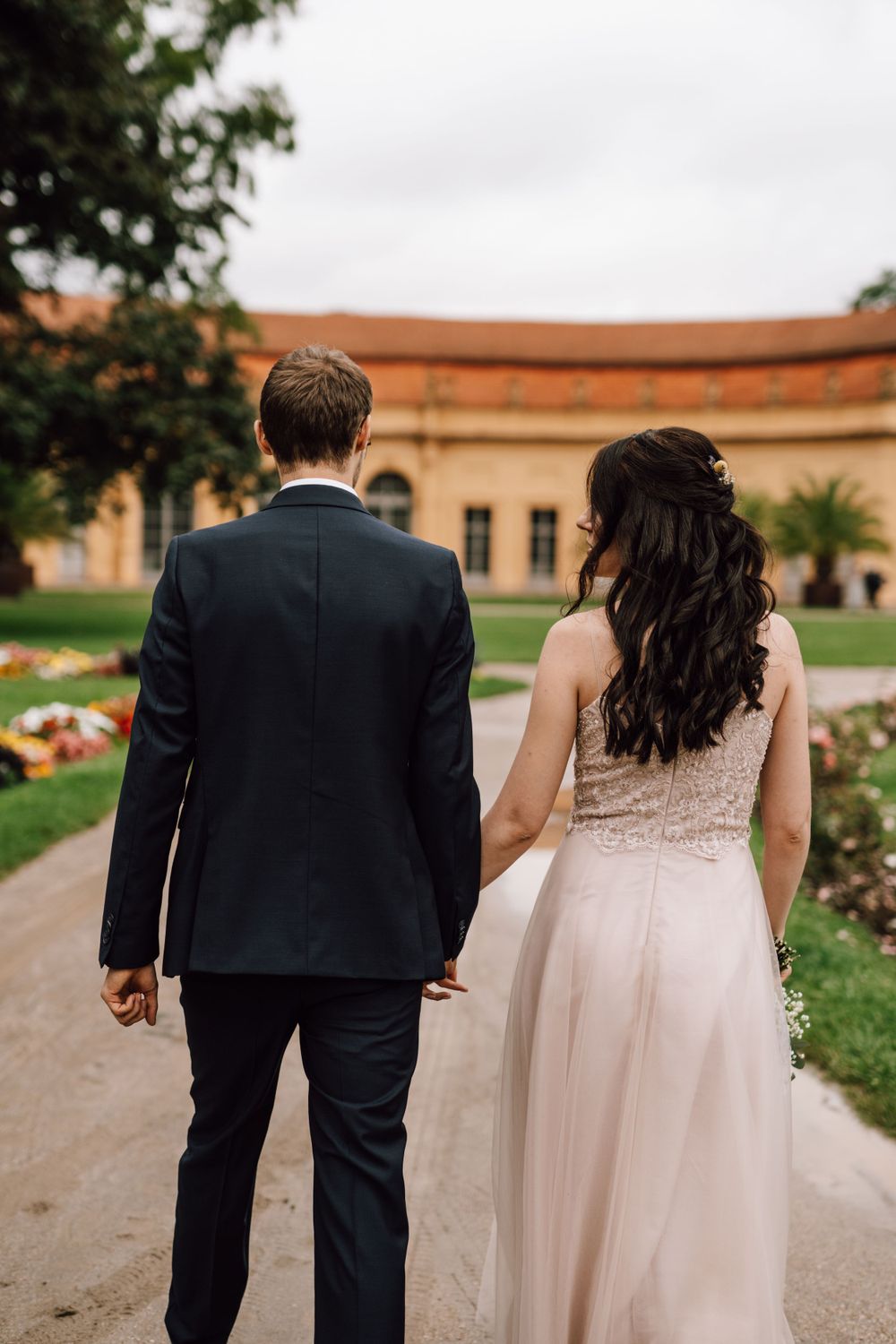 Couple walks hand in hand along a path by a historic building.