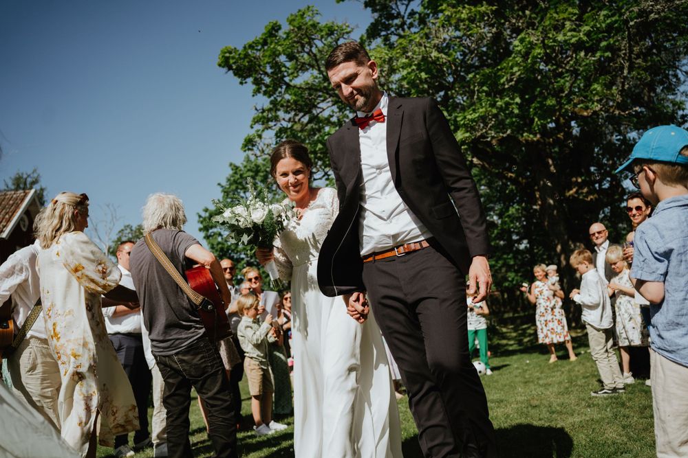 Wedding couple celebrates with guests on a sunny lawn during daytime reception.