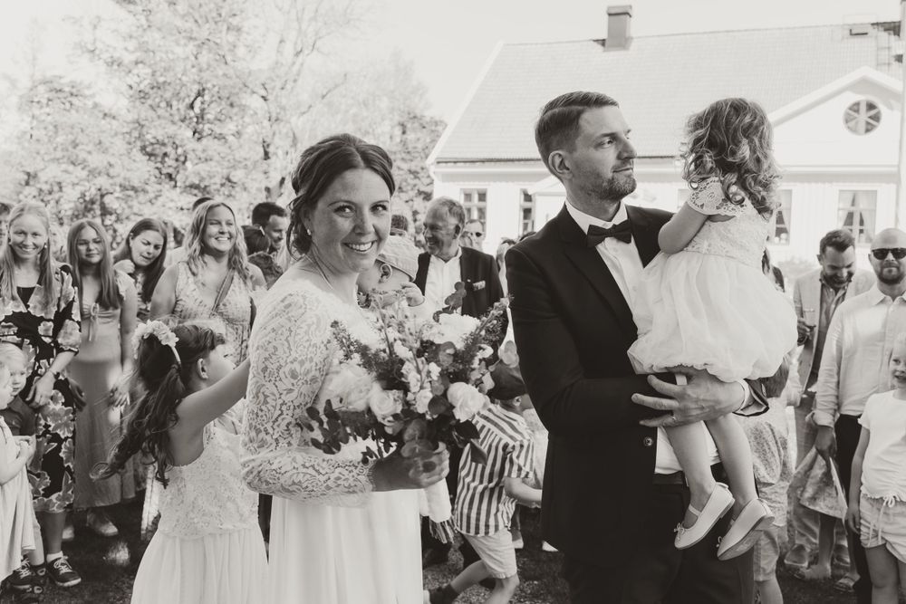 Wedding couple and child celebrate with guests during outdoor ceremony.