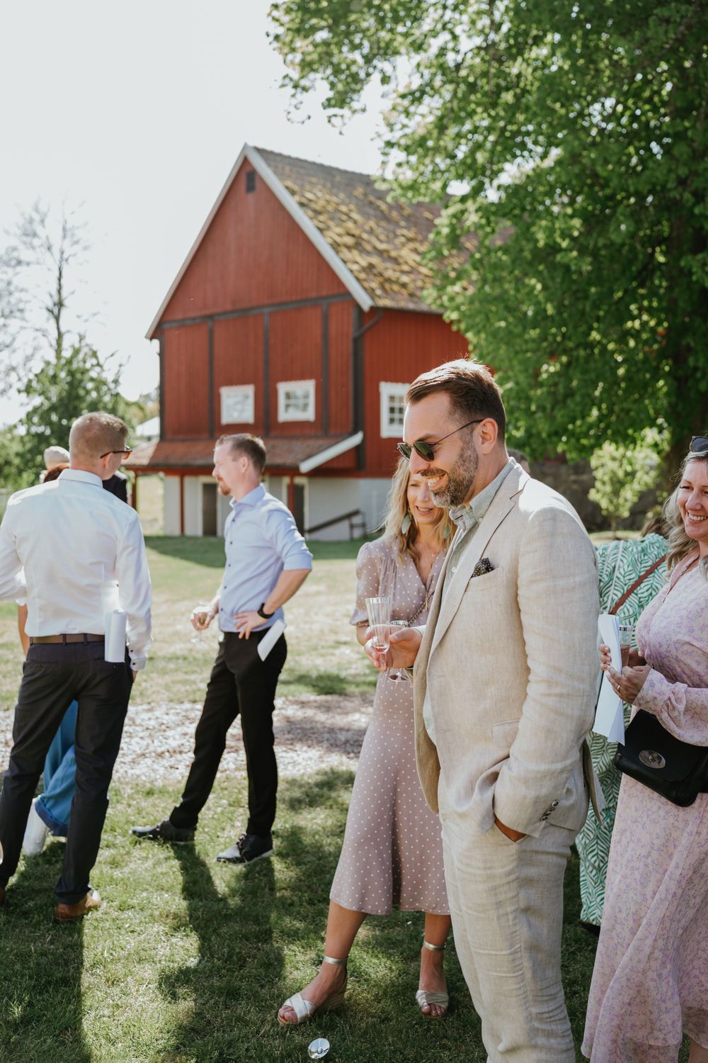 Wedding guests socialize on lawn with red barn in background.