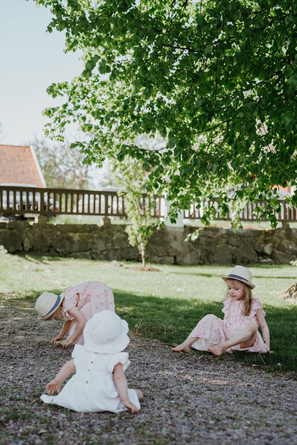 Children in pink and white dresses play on ground near stone wall.
