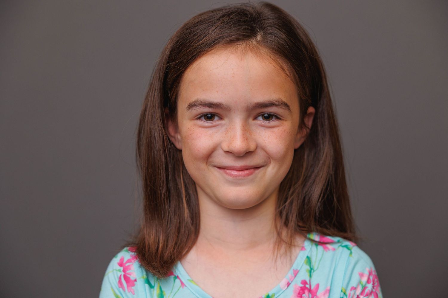 Young person in a floral print dress smiling warmly against a dark gray background.
