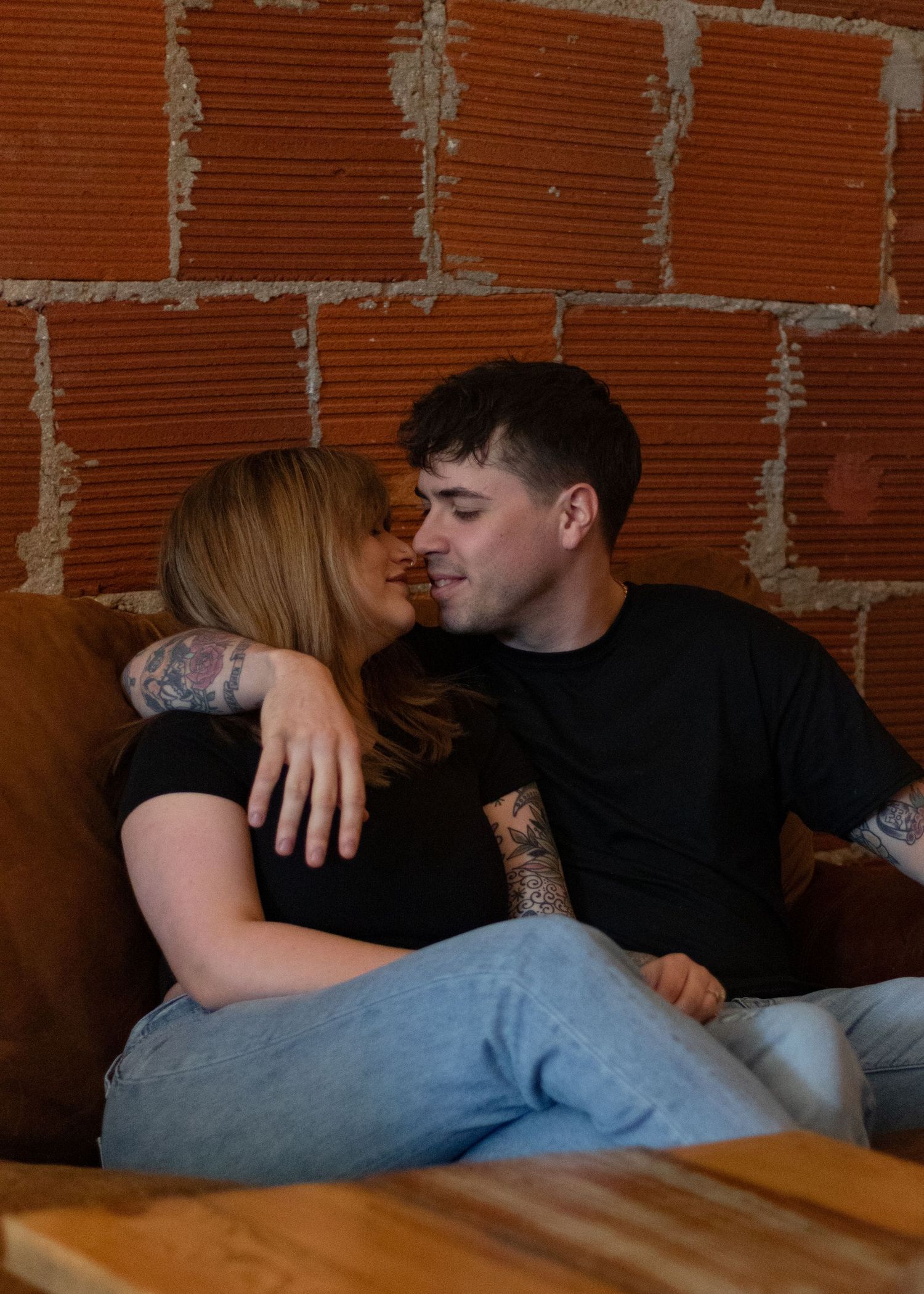 A couple sitting together against a rustic brick wall interior.